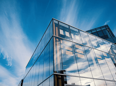 Modern glass office building exterior against a blue sky, viewed from a low angle.